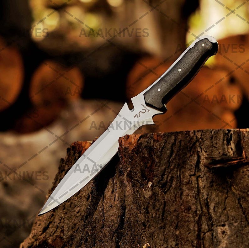 May include: A stainless steel hunting knife with a black handle and a silver blade. The knife is angled, resting on a tree stump. The handle has three silver rivets. The blade has a decorative design near the handle.
