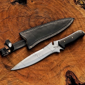 May include: A black leather-sheathed hunting knife with a black wooden handle and a silver blade. The blade has a serrated edge and a pointed tip.