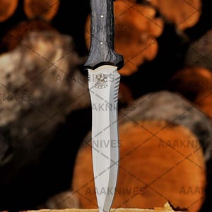 May include: A dagger with a dark wooden handle and a silver blade. The handle has a unique shape and is attached to a silver guard with a decorative emblem. The blade is sharp and pointed. The text "AAAKNIVES" is visible.
