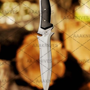 May include: A stainless steel knife with a black and silver handle. The blade is sharp and pointed. The handle has a textured grip with three white dots. The knife is standing upright on a wooden surface. The text "AAAKNIVES" is visible.