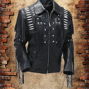 Könnte beinhalten: Schwarze Lederjacke mit Fransen und silberfarbenen Nieten. Die Jacke hat einen Reißverschluss, einen Reverskragen und weiße Akzente auf den Schultern. Die Ärmel und die Brust sind mit Fransen versehen, was einen klassischen Western-Look erzeugt.