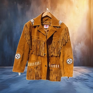 Könnte beinhalten: Braune Wildlederjacke mit Fransen an Brust, Taschen und Ärmeln. Die Jacke hat dekorative Perlenarbeiten an den Schultern und unteren Ärmeln. Sie hängt an einem Holzbügel.