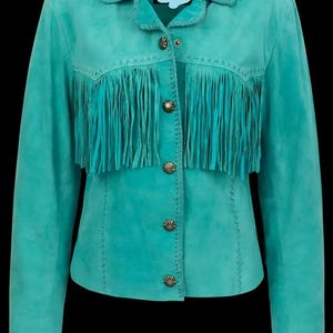 May include: Turquoise suede jacket with fringe detailing across the chest. The jacket features a collared neckline, decorative buttons, and long sleeves. The stitching is visible along the seams. A stylish western-inspired garment.