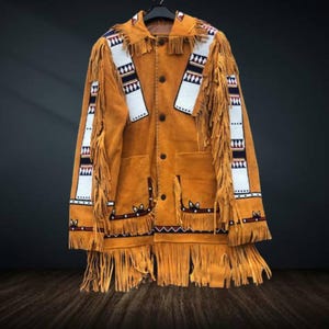 Könnte beinhalten: Eine hellbraune Wildlederjacke mit Fransen und dekorativen Perlen. Die Jacke hat einen Kragen, Knopfverschlüsse und zwei Vordertaschen. Weiße, rote und blaue Perlenakzente zieren die Ärmel und die Vorderseite.