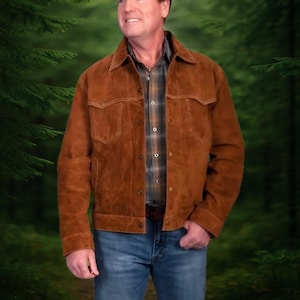 Könnte beinhalten: Braune Wildlederjacke mit Knopfleiste, zwei Brusttaschen und Kragen. Die Jacke wird über einem karierten Hemd und einer blauen Jeans getragen. Die Jacke ist ein klassischer Stil.