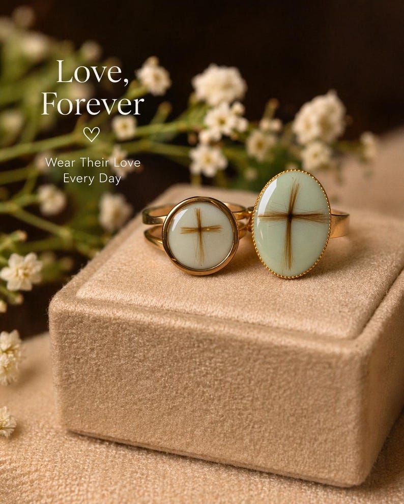 May include: Two gold rings with light green oval and round settings, each featuring a cross design made of brown hair. The rings sit on a beige velvet box, with the words "Love, Forever" and "Wear Their Love Every Day" in the background.