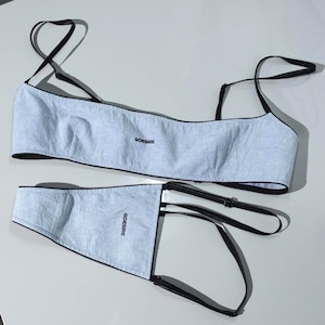 Peut inclure: Ensemble de lingerie deux pièces bleu clair. Le haut est de style bandeau avec de fines bretelles noires. Le bas est un slip taille haute. Le texte "QDESIRE" est imprimé sur les deux pièces. L'ensemble est en matière réfléchissante.