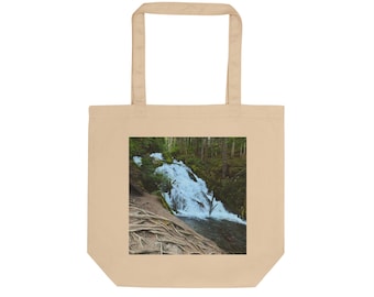 May include: Beige tote bag featuring a scenic image of a waterfall cascading through a lush forest. The image is framed within a square on the front of the bag. The bag has two handles for carrying.