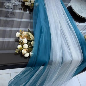 May include: A teal and white tulle table runner with white flowers on a dark wood table.