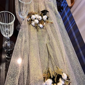 Puede incluir: Un camino de mesa blanco transparente con un acabado brillante. Tres ramos de rosas blancas se colocan en el camino de mesa. Dos copas de vidrio transparente también están en el camino de mesa.