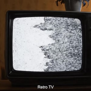 Puede incluir: Un televisor negro retro con una pantalla que muestra estática. El texto "Retro TV" es visible en la parte inferior. Una mano gira un mando en el lateral. El televisor está sobre una superficie de madera.