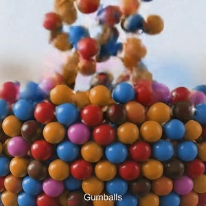 May include: A clear glass bowl filled with colorful gumballs. The gumballs are in various colors, including red, blue, orange, brown, and pink. The word "Gumballs" is at the bottom of the image.