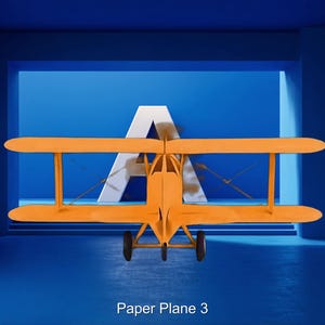 May include: An orange biplane model with black wheels is centered against a blue backdrop with a large white "A". The text "Paper Plane 3" is at the bottom. The biplane has two wings and a propeller.