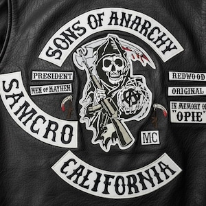 May include: Black leather jacket with patches. The patches include the words "Sons of Anarchy", "SAMCRO", "California", and "Redwood Original". A central patch features a grim reaper with a scythe and a gun. The jacket also has patches that say "President", "Men of Mayhem", "In Memory of Opie", and "MC".