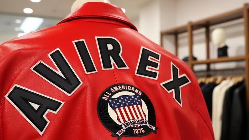 May include: Red leather jacket with the word "AVIREX" in large black letters outlined in white on the back. A circular patch with the American flag and the text "ALL AMERICANS ESTABLISHED 1975" is also visible.