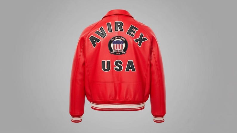 May include: Red leather jacket with white and red striped cuffs and hem. The back features the text "AVIREX" above "USA" and a circular patch with a flag design. A classic bomber jacket style.