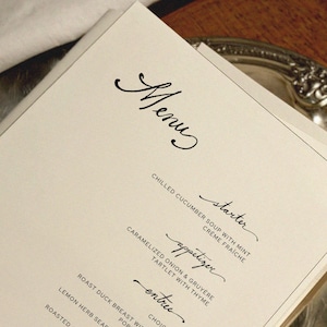 Puede incluir: Un menú impreso en papel color crema con elegante escritura negra. La palabra "Menu" está en la parte superior, seguida de nombres de platos como "starter" y "appetizer". Los platos incluyen sopa de pepino y tartaleta de cebolla caramelizada.