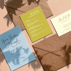 May include: Wedding stationery set featuring a blue invitation card with the text "We're Getting Married", a green details card, and a cream RSVP card. Brown envelopes are also included.