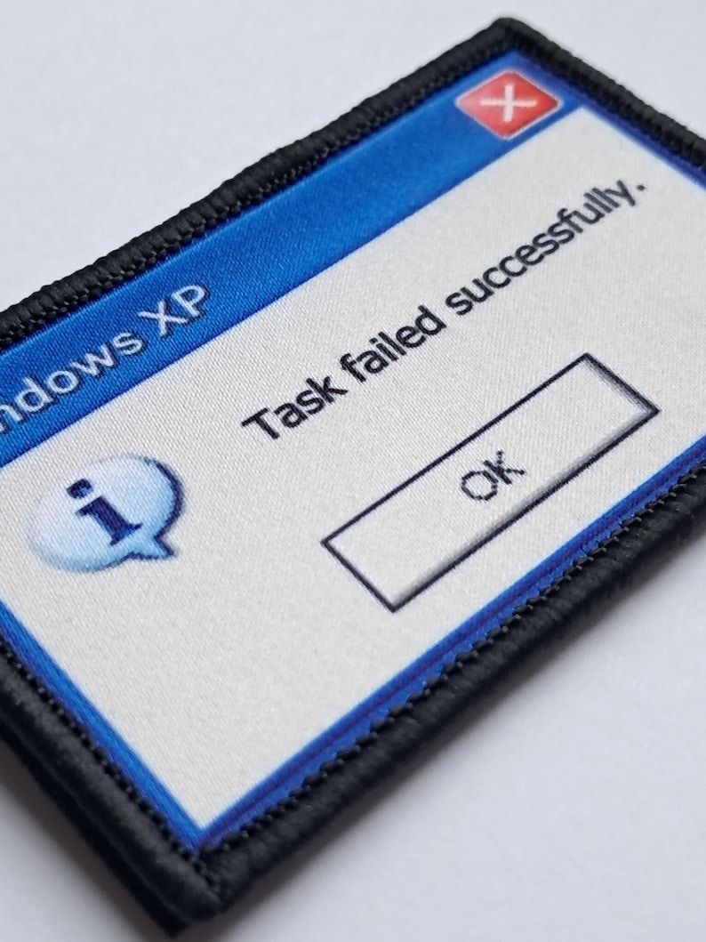 Pu&ograve; includere: Una toppa rettangolare con bordo nero e design blu e bianco. La toppa presenta un messaggio di errore in stile Windows XP che recita "Task failed successfully." con un pulsante "OK".