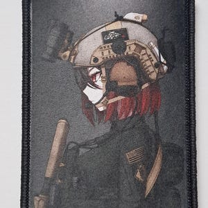 Può includere: Una toppa rettangolare con bordo nero presenta un'illustrazione in stile anime di una figura in equipaggiamento tattico. La figura indossa un elmetto color cachi con accessori dettagliati e ha i capelli rossi. È visibile una toppa con la bandiera americana.