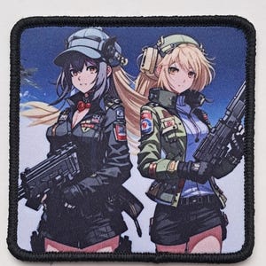 Può includere: Toppa quadrata con un'illustrazione in stile anime di due donne in uniforme militare, ognuna con un'arma da fuoco. Le donne hanno i capelli lunghi e indossano cappelli. La toppa ha un bordo nero.
