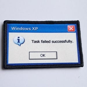 Pu&ograve; includere: Toppa ricamata con un messaggio di errore di Windows XP. La toppa ha una barra superiore blu con "Windows XP" e un'icona rossa "X". Il messaggio recita "Task failed successfully." con un pulsante "OK".