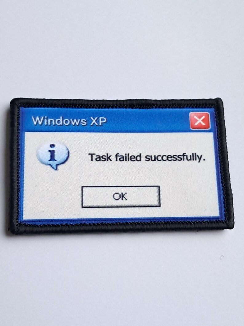 Pu&ograve; includere: Toppa ricamata con un messaggio di errore di Windows XP. La toppa ha una barra superiore blu con "Windows XP" e un'icona rossa "X". Il messaggio recita "Task failed successfully." con un pulsante "OK".