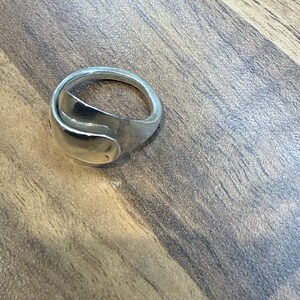 May include: A silver ring with a unique, curved design. The ring has a smooth, polished finish and a modern aesthetic. The ring is a piece of jewelry.