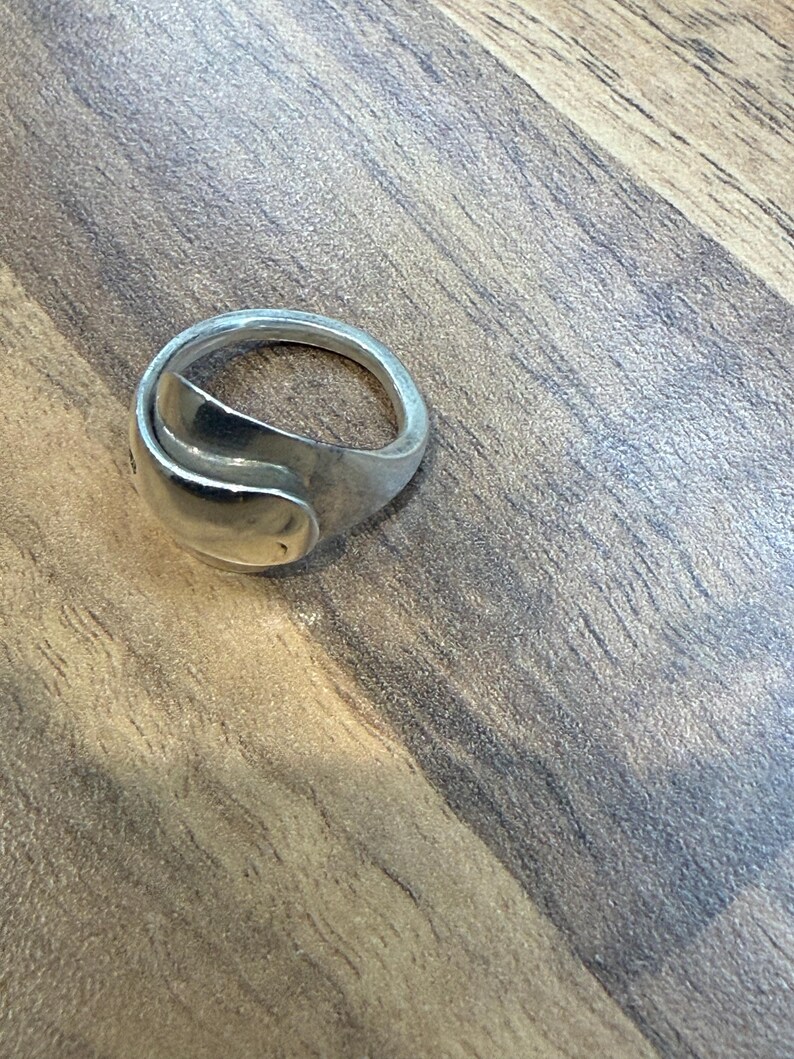 May include: A silver ring with a unique, curved design. The ring has a smooth, polished finish and a modern aesthetic. The ring is a piece of jewelry.
