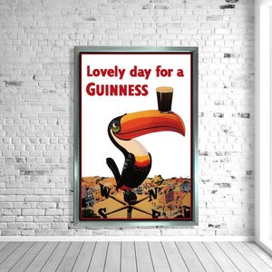 K&ouml;nnte beinhalten: Gerahmtes Vintage-Guinness-Poster mit einem Tukan mit gro&szlig;em orange-rotem Schnabel, der ein Pint Guinness h&auml;lt. Der Text lautet "Lovely day for a Guinness" in Rot und Schwarz. Der Hintergrund zeigt eine Stadtansicht.
