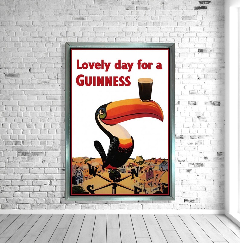 K&ouml;nnte beinhalten: Gerahmtes Vintage-Guinness-Poster mit einem Tukan mit gro&szlig;em orange-rotem Schnabel, der ein Pint Guinness h&auml;lt. Der Text lautet "Lovely day for a Guinness" in Rot und Schwarz. Der Hintergrund zeigt eine Stadtansicht.