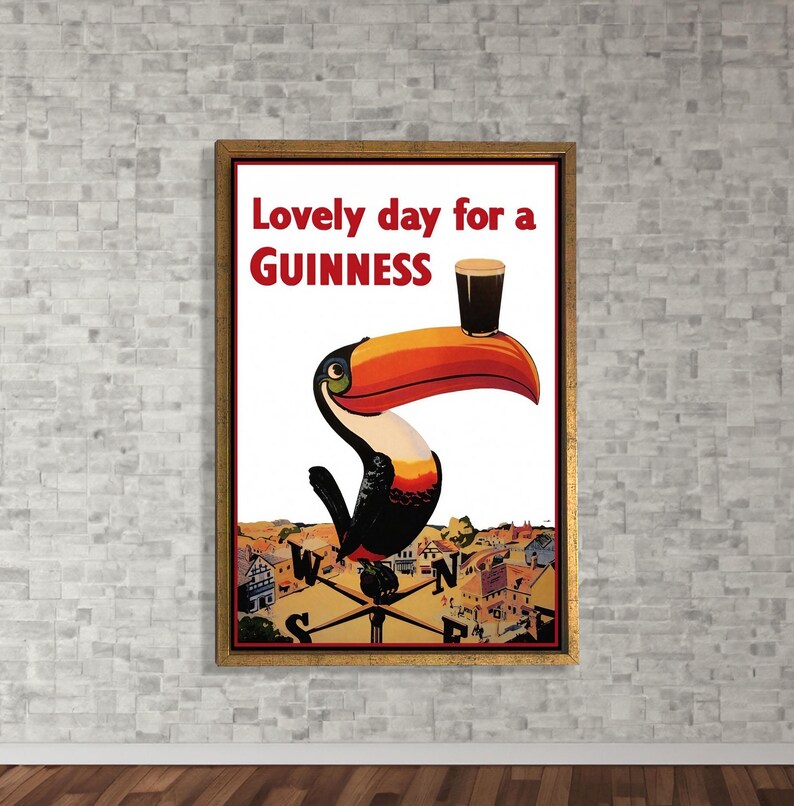 K&ouml;nnte beinhalten: Gerahmtes Vintage-Guinness-Poster mit einem Tukan, der ein Pint Guinness auf dem Schnabel balanciert. Der Text "Lovely day for a Guinness" ist in Rot und Wei&szlig;. Der Hintergrund zeigt eine Stadt und einen Kompass.