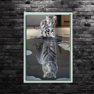 Könnte beinhalten: Gerahmter Druck mit einer Katze, die in Wasser steht, und ihrem Spiegelbild, das als Tiger erscheint. Die Katze hat grau-schwarze Streifen, während das Tiger-Spiegelbild weiß mit schwarzen Streifen ist. Der Rahmen ist hellgrün, der Hintergrund eine Backsteinmauer.