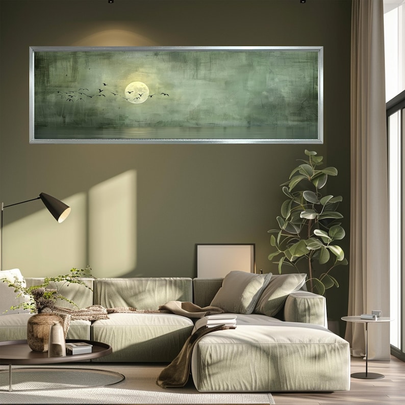 Puede incluir: Una gran obra de arte rectangular enmarcada representa un paisaje sereno con una luna llena y p&aacute;jaros silueteados en vuelo. La obra de arte tiene una paleta de colores verde y gris apagados, creando una atm&oacute;sfera relajante. El marco es plateado.