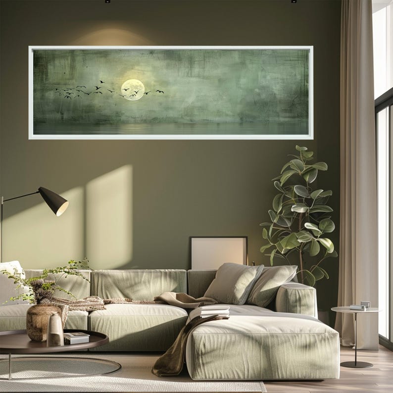 Puede incluir: Una pintura de paisaje enmarcada representa una luna llena y aves silueteadas sobre un fondo verde y gris apagado. La obra de arte cuelga sobre un sof&aacute; seccional verde claro en un sal&oacute;n moderno.