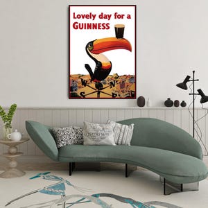 K&ouml;nnte beinhalten: Ein gerahmtes Vintage-Werbeplakat f&uuml;r Guinness mit einem Tukan, der ein Pint Stout auf seinem Schnabel balanciert. Der Text "Lovely day for a Guinness" ist rot. Das Kunstwerk hat einen Retro-Stil.