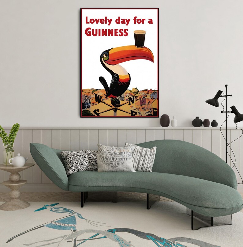 K&ouml;nnte beinhalten: Ein gerahmtes Vintage-Werbeplakat f&uuml;r Guinness mit einem Tukan, der ein Pint Stout auf seinem Schnabel balanciert. Der Text "Lovely day for a Guinness" ist rot. Das Kunstwerk hat einen Retro-Stil.