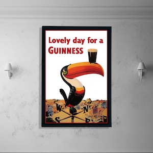 K&ouml;nnte beinhalten: Gerahmtes Vintage-Guinness-Werbeplakat mit einem Tukan, der ein Pint Guinness auf seinem Schnabel balanciert. Das Poster tr&auml;gt den roten Text "Lovely day for a Guinness". Der Tukan ist schwarz, wei&szlig;, orange und gelb, vor wei&szlig;em Hintergrund.