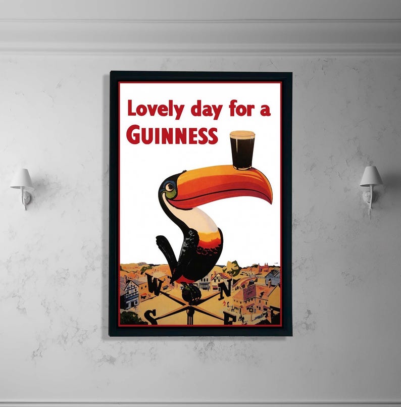 K&ouml;nnte beinhalten: Gerahmtes Vintage-Guinness-Werbeplakat mit einem Tukan, der ein Pint Guinness auf seinem Schnabel balanciert. Das Poster tr&auml;gt den roten Text "Lovely day for a Guinness". Der Tukan ist schwarz, wei&szlig;, orange und gelb, vor wei&szlig;em Hintergrund.
