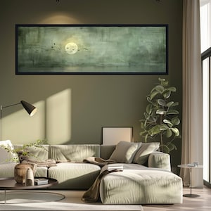 Puede incluir: Una pintura de paisaje enmarcada representa una luna llena y p&aacute;jaros silueteados sobre un fondo verde y gris apagado. La obra de arte cuelga sobre un sof&aacute; seccional verde claro en un sal&oacute;n moderno. Tambi&eacute;n se ven una planta alta y una mesa de centro redonda.
