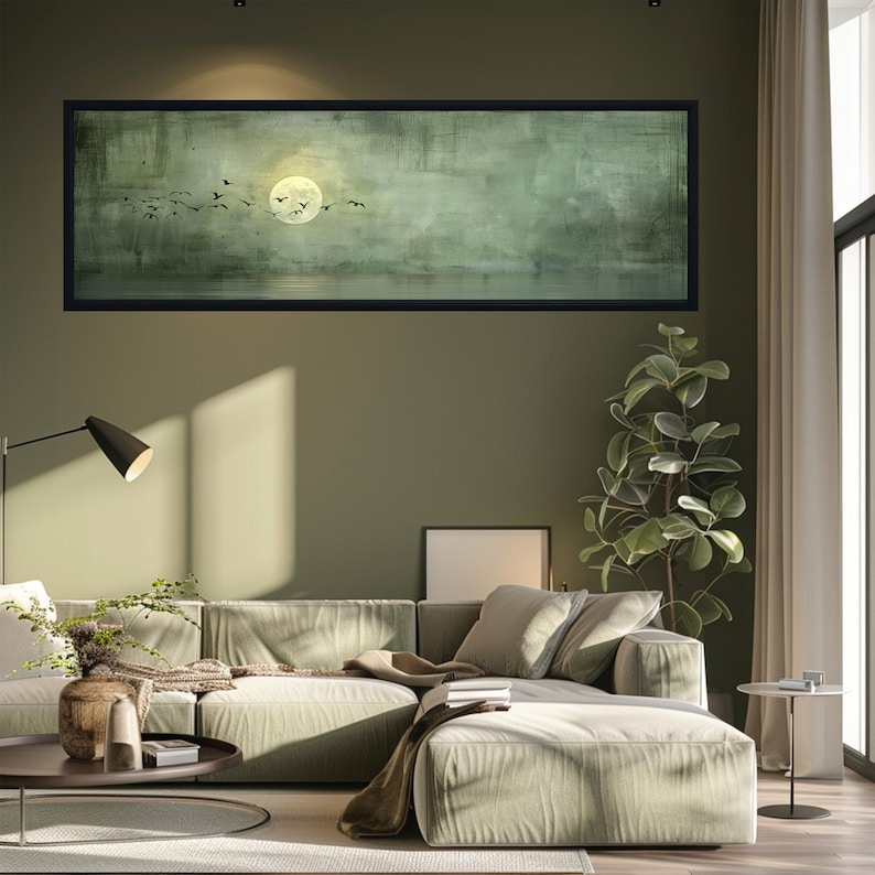 Puede incluir: Una pintura de paisaje enmarcada representa una luna llena y p&aacute;jaros silueteados sobre un fondo verde y gris apagado. La obra de arte cuelga sobre un sof&aacute; seccional verde claro en un sal&oacute;n moderno. Tambi&eacute;n se ven una planta alta y una mesa de centro redonda.