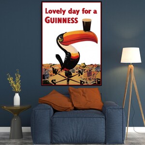 K&ouml;nnte beinhalten: Gerahmtes Vintage-Guinness-Poster mit einem Tukan, der ein Pint Guinness auf seinem Schnabel balanciert. Der Text lautet "Lovely day for a Guinness". Der Tukan ist vor dem Hintergrund einer Stadt und eines Kompasses platziert.