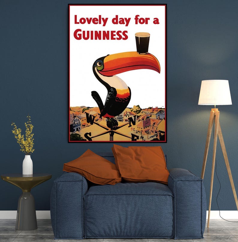 K&ouml;nnte beinhalten: Gerahmtes Vintage-Guinness-Poster mit einem Tukan, der ein Pint Guinness auf seinem Schnabel balanciert. Der Text lautet "Lovely day for a Guinness". Der Tukan ist vor dem Hintergrund einer Stadt und eines Kompasses platziert.
