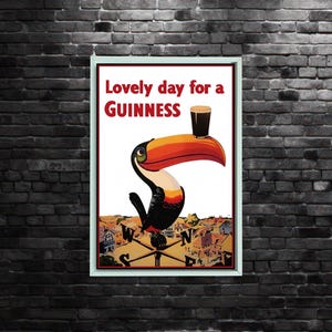 K&ouml;nnte beinhalten: Gerahmtes Vintage-Guinness-Poster mit einem Tukan, der ein Pint Guinness auf seinem Schnabel balanciert. Das Poster tr&auml;gt die Aufschrift "Lovely day for a Guinness". Der Tukan ist schwarz, wei&szlig;, orange und gelb, mit einer Stadtansicht im Hintergrund.