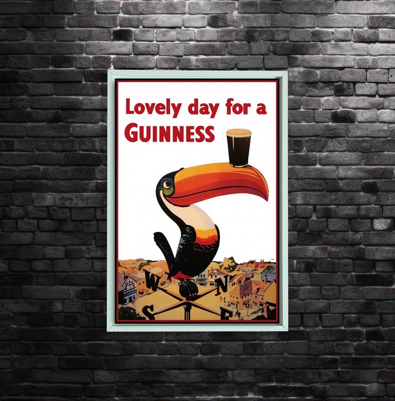 K&ouml;nnte beinhalten: Gerahmtes Vintage-Guinness-Poster mit einem Tukan, der ein Pint Guinness auf seinem Schnabel balanciert. Das Poster tr&auml;gt die Aufschrift "Lovely day for a Guinness". Der Tukan ist schwarz, wei&szlig;, orange und gelb, mit einer Stadtansicht im Hintergrund.