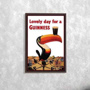 K&ouml;nnte beinhalten: Gerahmter Druck mit einem Tukan, der ein Guinness-Bier h&auml;lt. Der Text "Lovely day for a Guinness" ist rot. Der Tukan befindet sich &uuml;ber einer Stadtlandschaft und einer Windrose. Das Kunstwerk hat einen Vintage-Poster-Stil.
