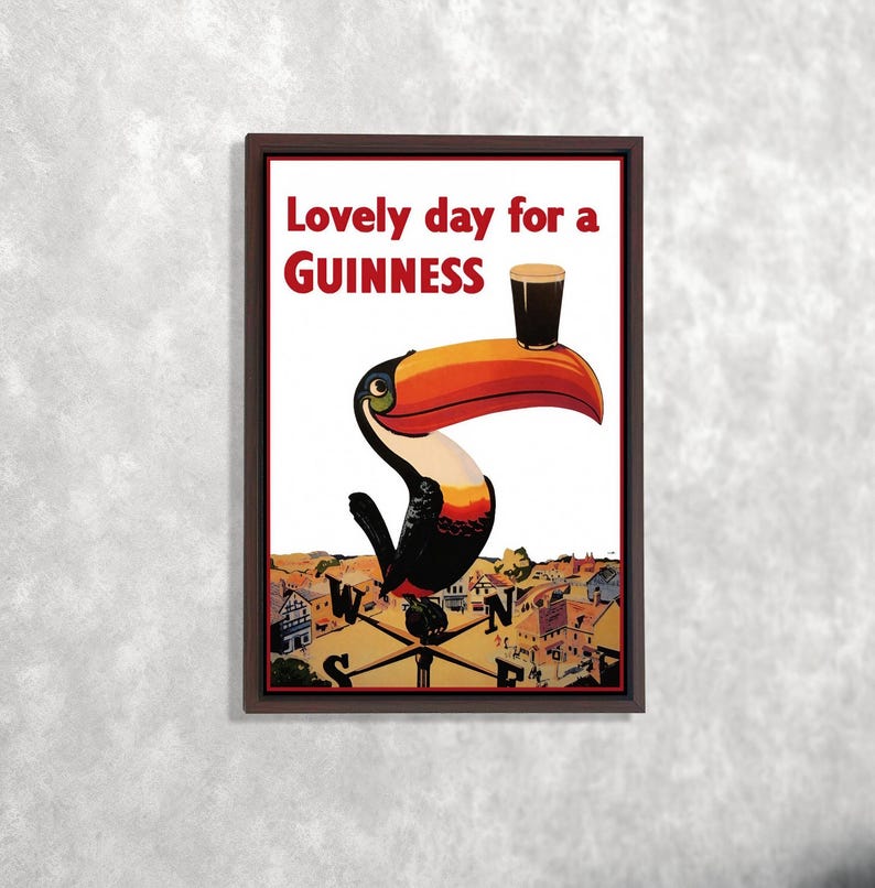 K&ouml;nnte beinhalten: Gerahmter Druck mit einem Tukan, der ein Guinness-Bier h&auml;lt. Der Text "Lovely day for a Guinness" ist rot. Der Tukan befindet sich &uuml;ber einer Stadtlandschaft und einer Windrose. Das Kunstwerk hat einen Vintage-Poster-Stil.