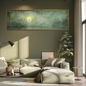 Puede incluir: Una obra de arte rectangular enmarcada que representa un paisaje sereno con una luna llena y p&aacute;jaros volando. La obra de arte, en tonos verdes y dorados, cuelga sobre un sof&aacute; seccional verde claro en una sala de estar moderna.
