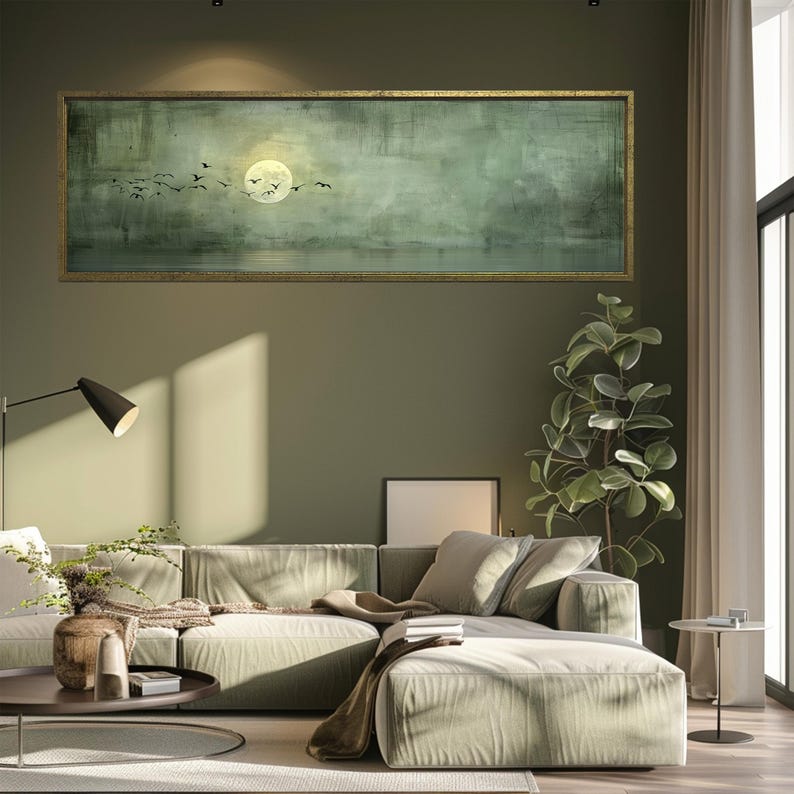 Puede incluir: Una obra de arte rectangular enmarcada que representa un paisaje sereno con una luna llena y p&aacute;jaros volando. La obra de arte, en tonos verdes y dorados, cuelga sobre un sof&aacute; seccional verde claro en una sala de estar moderna.