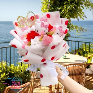 Peut inclure: Un bouquet de fleurs roses et rouges enveloppé dans du papier blanc à pois rouges. Le bouquet comprend trois peluches Hello Kitty.